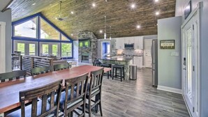 A spacious kitchen with a stone fireplace, a dining area with a large wooden table and chairs, and a view of the outdoors through large windows. - Lake Effect on Norris Lake (New Tazewell)