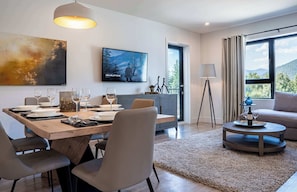 A modern dining area with a wooden table, chairs, and a television mounted on the wall. - The Stoke Stopover - Revelstoke Condo with Hot Tub (Revelstoke)
