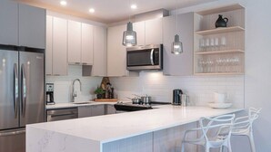 A modern kitchen with stainless steel appliances, white cabinetry, a marble island, and pendant lighting. - The Stoke Stopover - Revelstoke Condo with Hot Tub (Revelstoke)