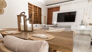 A modern dining area with a wooden table, woven placemats, and a large TV mounted on the wall. - Casa Don Toribio: Luxury Home with Private Pool (Aguada)