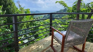A wicker chair on a wooden deck with a metal railing, overlooking a lush green landscape and a clear blue sky. - Casa Don Toribio: Luxury Home with Private Pool (Aguada)