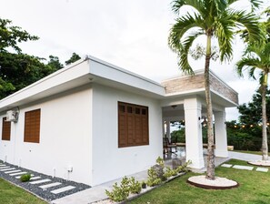 A modern house with a white exterior, wooden shutters, and a small garden with a palm tree. - Casa Don Toribio: Luxury Home with Private Pool (Aguada)