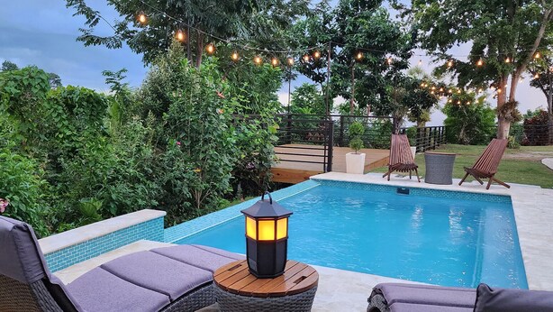 A swimming pool with lounge chairs and a lantern, surrounded by greenery and string lights. - Casa Don Toribio: Luxury Home with Private Pool (Aguada)
