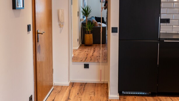 A hallway with a wooden floor, a black refrigerator, and a door with a mirror. - M Apartment: Feel good in the charming apartment (Landau in der Pfalz)
