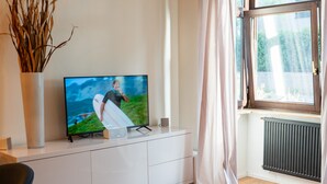 A modern living room with a flat-screen TV on a white cabinet, a glass bottle, a remote control, and a vase with dried plants. - M Apartment: Feel good in the charming apartment (Landau in der Pfalz)