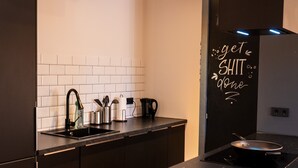 A modern kitchen with dark cabinetry, a black countertop, and a backsplash of white tiles. - M Apartment: Feel good in the charming apartment (Landau in der Pfalz)