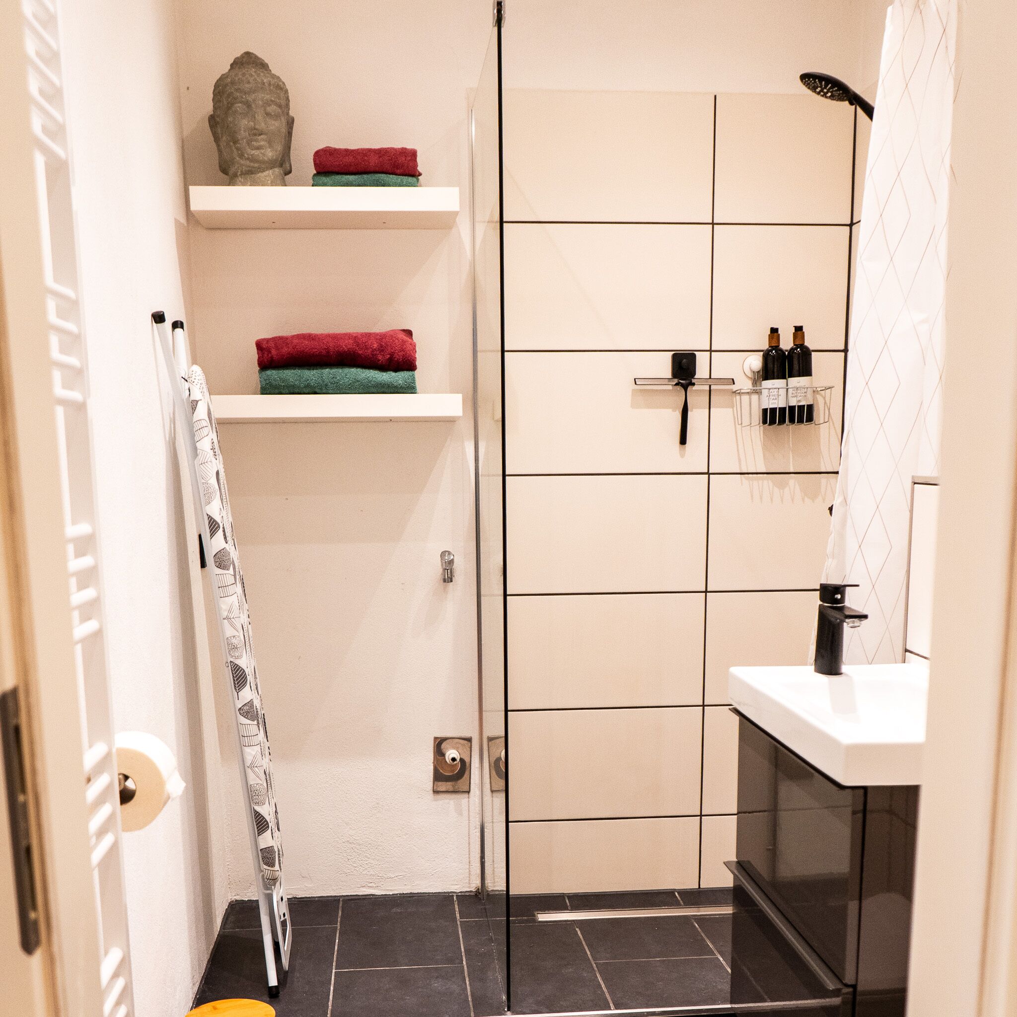 A bathroom with a shower, a toilet, a sink, and shelves with towels and toiletries.
