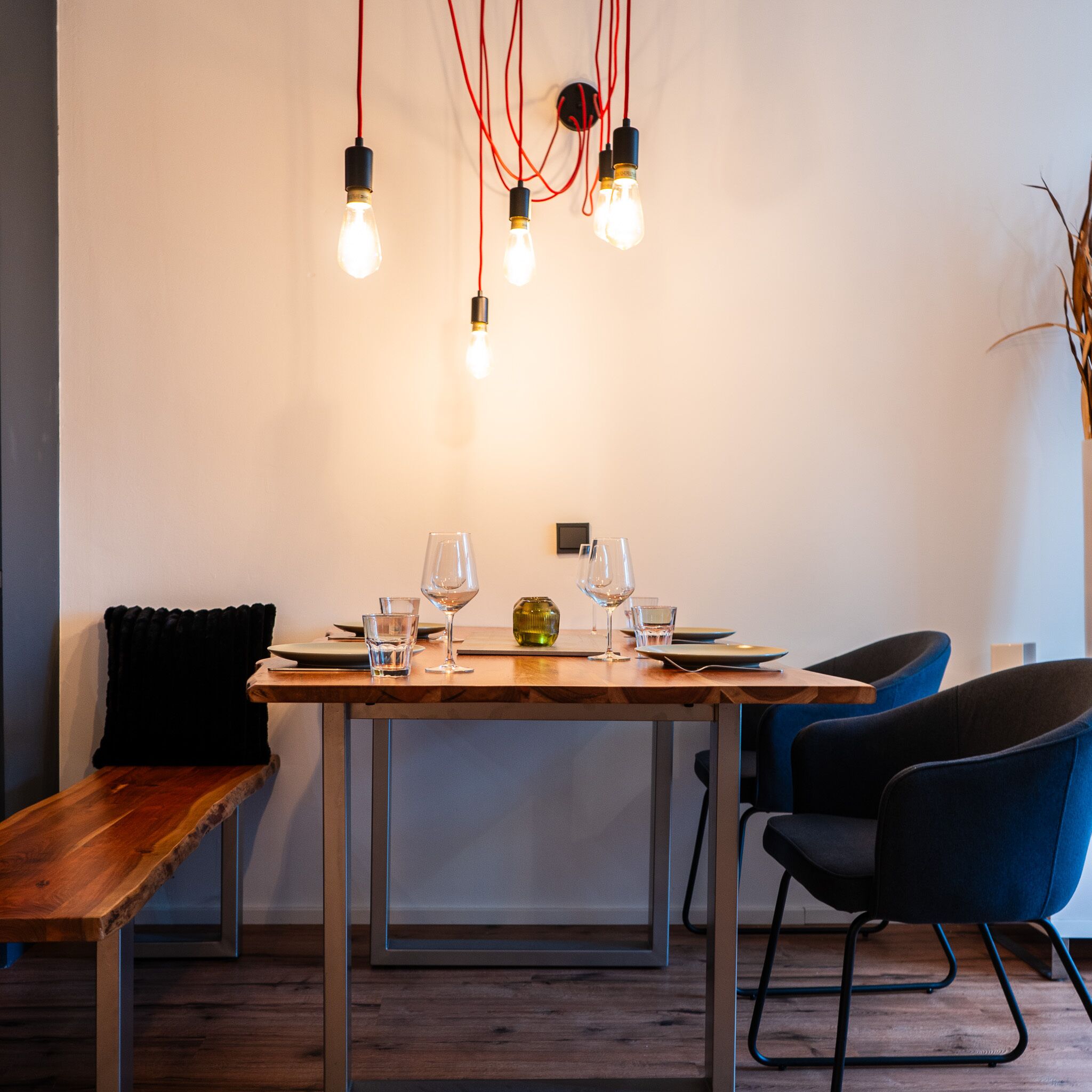 Un comedor con una mesa de madera dispuesta para dos personas, un banco y dos sillas.