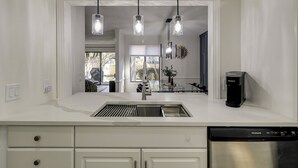 A modern kitchen with a stainless steel sink, a built-in dishwasher, and pendant lights.