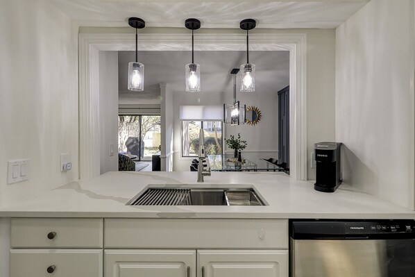 A modern kitchen with a stainless steel sink, a built-in dishwasher, and pendant lights.