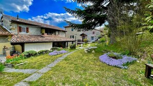 A stone building with a tiled roof, a stone pathway, and a garden with purple flowers. - Mazzetti Country House-Country living and garden (Collina di Savignano)