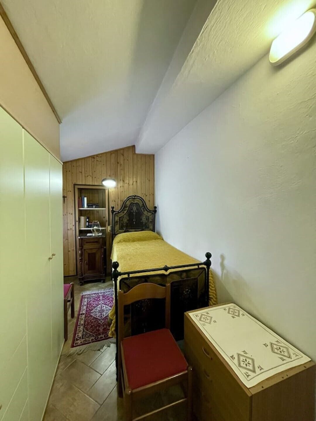 Ein kleines Schlafzimmer mit einem Einzelbett, einem Holzschrank, einem kleinen Tisch und einem Schreibtisch.