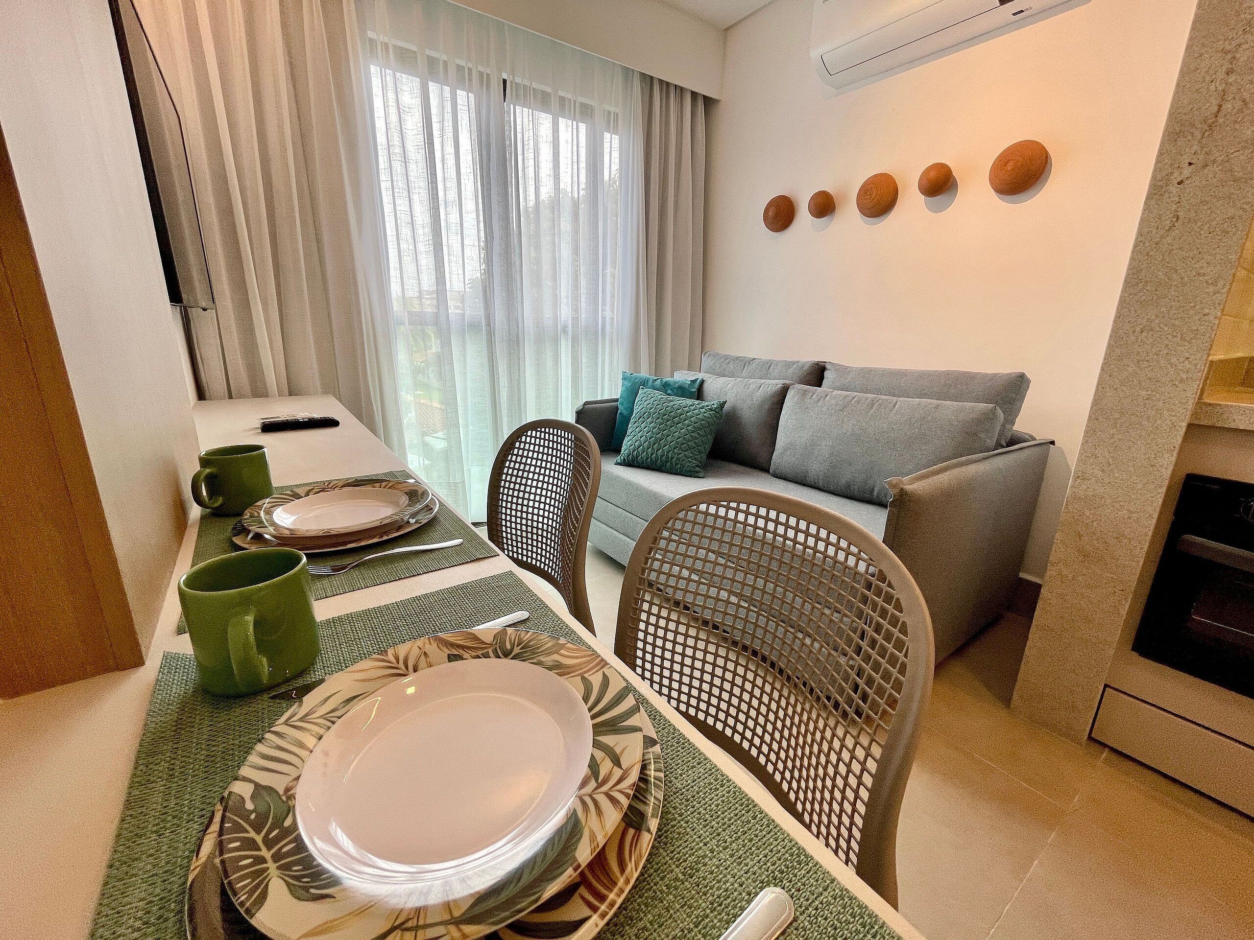 Un coin repas avec une table dressée pour deux personnes, un canapé et un espace cuisine.