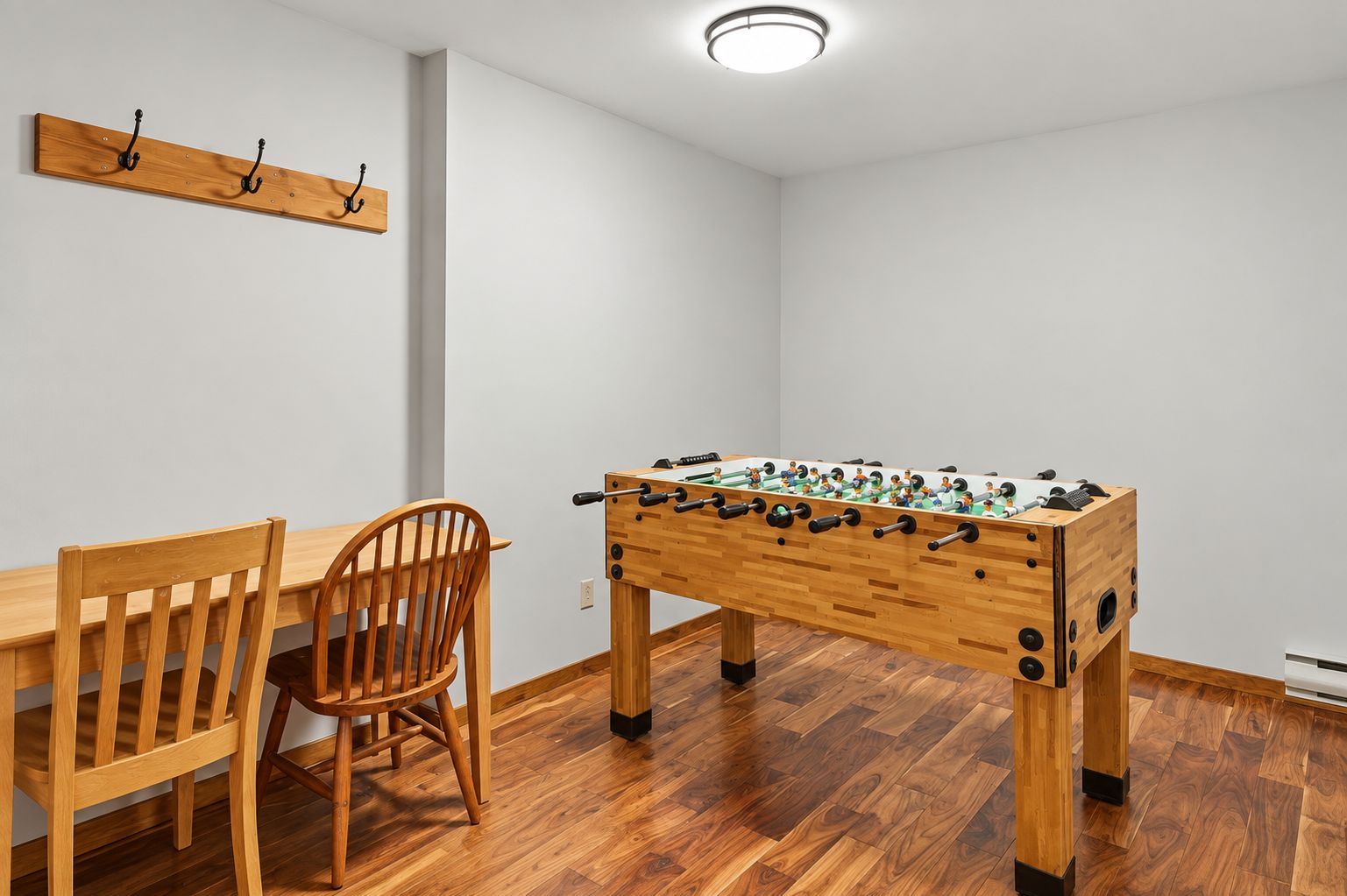 A room with a wooden foosball table, a wooden dining table, and a wooden chair.
