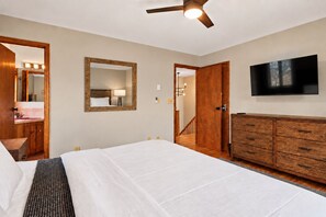 Een hotelkamer met een bed, een houten dressoir, een televisie, een spiegel en een badkamer zichtbaar door een geopende deur.