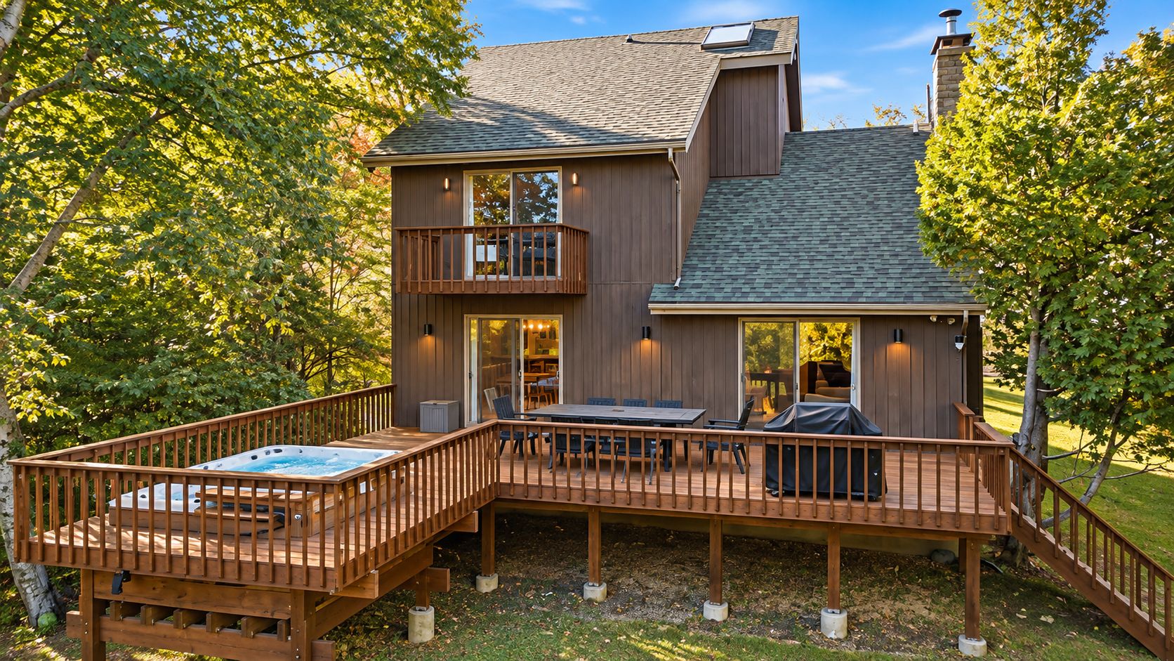 A two-story wooden house with a deck, a hot tub, and a covered outdoor seating area.