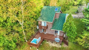 A two-story house with a green roof, a wooden deck, and a swimming pool.