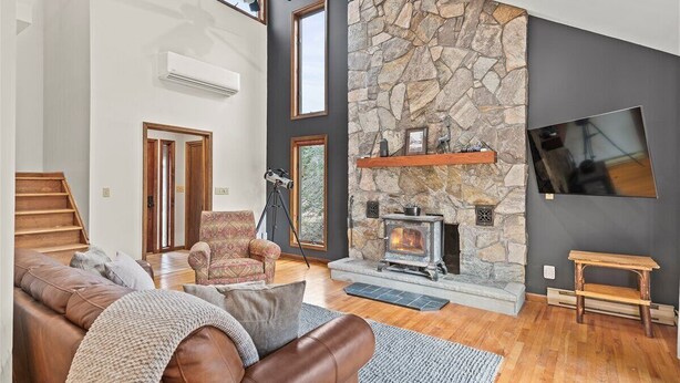 A spacious living room with a stone fireplace, a large TV mounted on the wall, and a cozy seating area with a leather couch and armchairs.