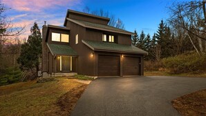 A modern two-story house with a garage, surrounded by trees and a driveway.