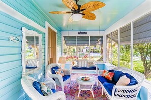 A covered porch with wicker furniture, a ceiling fan, and a view of the outdoors.