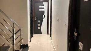 Un pasillo con una escalera a la izquierda, una puerta negra con un diseño blanco y negro en el centro, y otra puerta negra a la derecha.