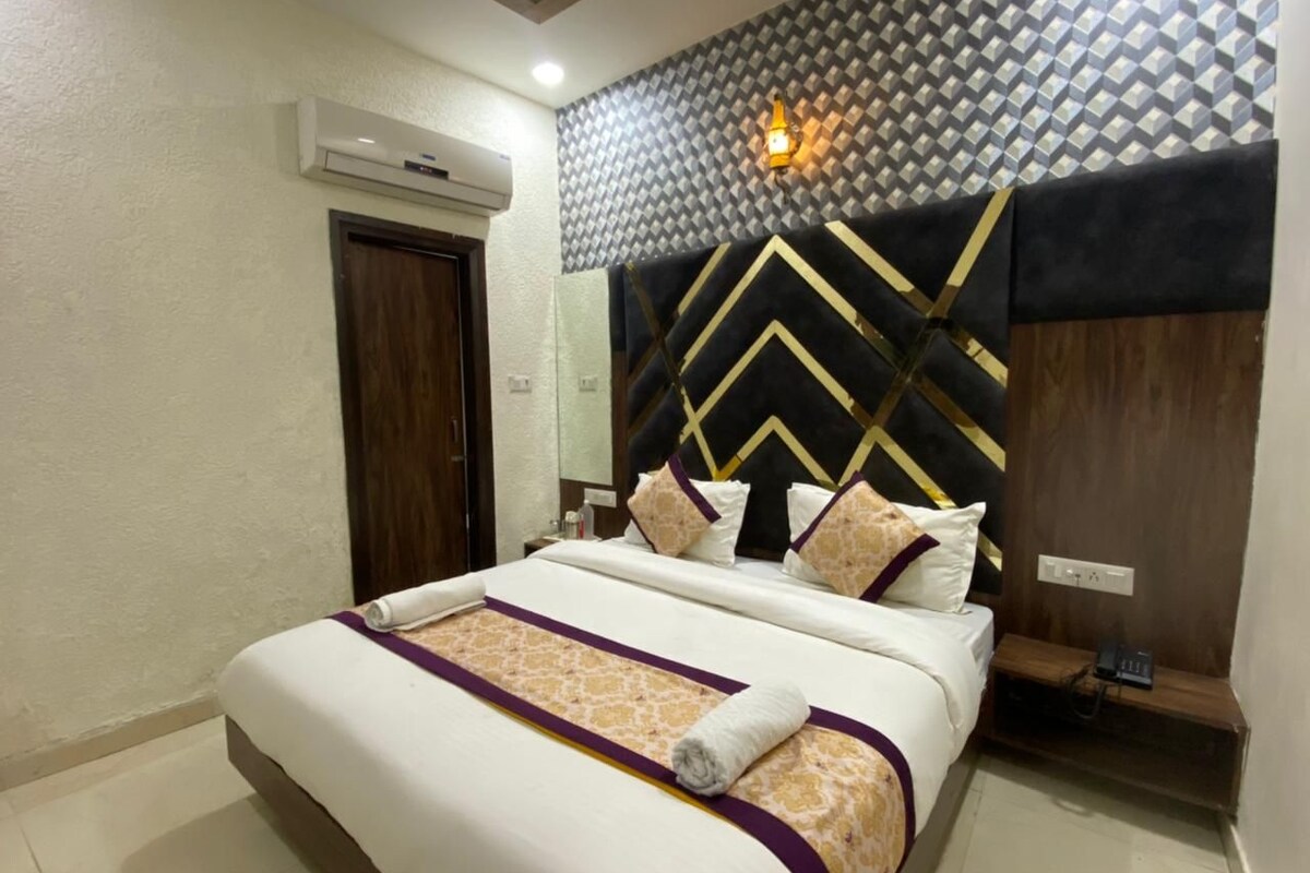 A neatly made bed with a patterned bedspread and pillows, a wall-mounted air conditioner, a wooden door, and a decorative wall panel.