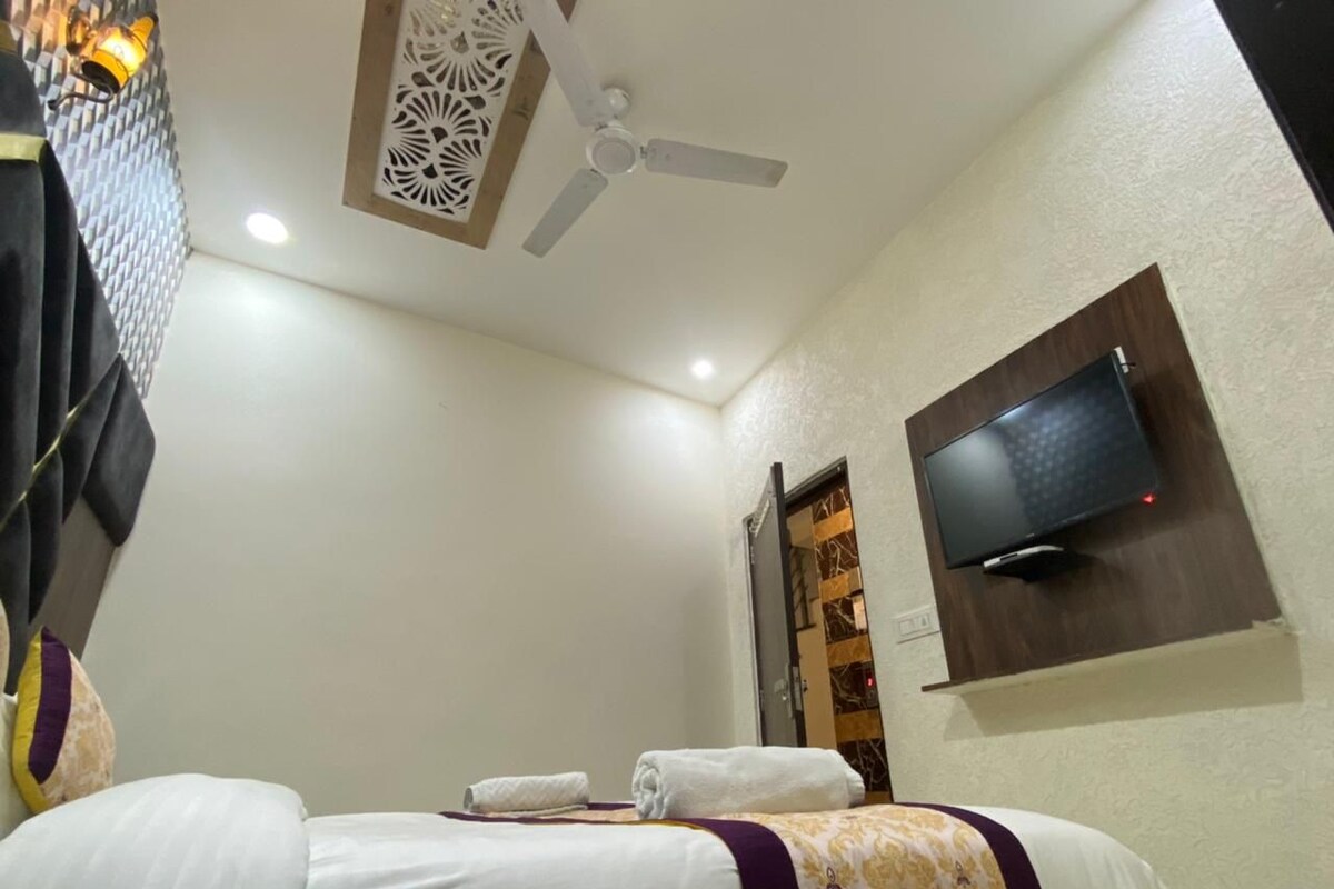 A hotel room with a bed, a ceiling fan, a flat-screen TV mounted on the wall, and a decorative wall panel.