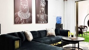 A modern living room with a black sectional sofa, a coffee table, and two large black-and-white framed artworks on the wall. - Lux Suites Gold Park Apartments Kilimani (Nairobi)