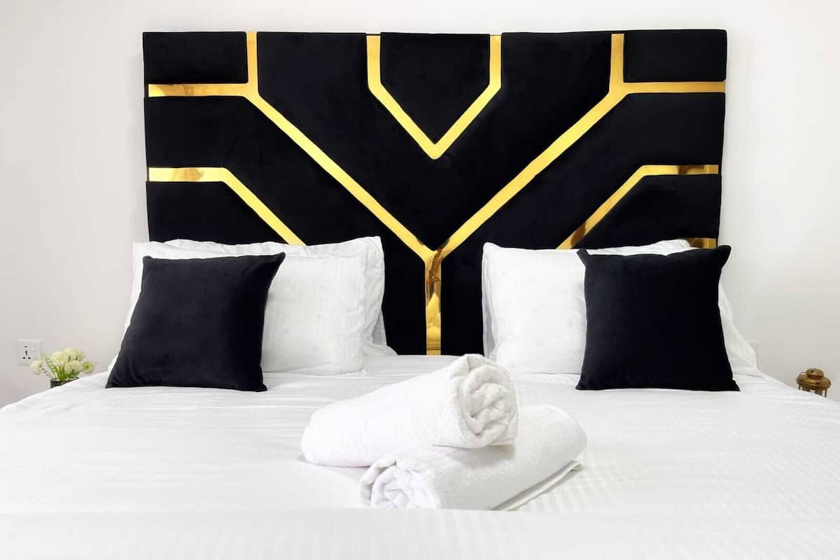 Una habitación de hotel con una cama grande, ropa de cama blanca y un cabecero negro y dorado.