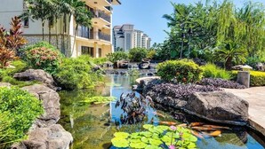 A serene garden with a pond, lush greenery, and a building in the background. - Summer Reduced! OT-503 Gorgeous Ocean and Pool View Villa! (Kapolei)
