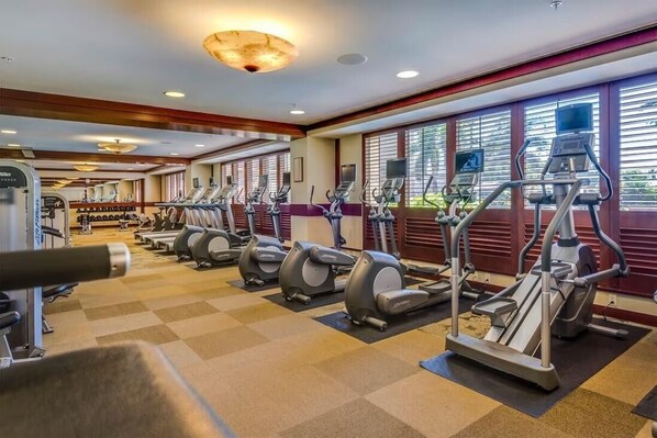 A gym with multiple treadmills and elliptical machines, a weight bench, and a wall-mounted TV.
