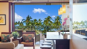 A balcony with a view of palm trees and the ocean, furnished with a sofa, chairs, and a small table. - Summer Reduced! OT-503 Gorgeous Ocean and Pool View Villa! (Kapolei)