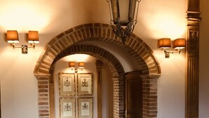 Un couloir voûté aux murs de briques, une porte en bois et des tableaux encadrés accrochés au mur.