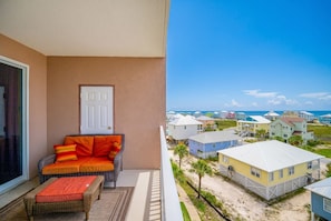 A balcony with a wicker sofa and ottoman, a door, and a view of beach houses. - The Dunes 503 1 Bedroom Condo (Gulf Shores)