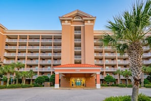 A multi-story hotel with a central entrance, balconies, and palm trees. - The Dunes 503 1 Bedroom Condo (Gulf Shores)