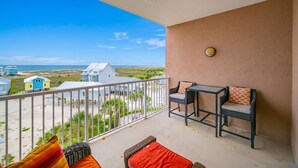 A balcony with a view of the beach, a table with chairs, and a small rug. - The Dunes 503 1 Bedroom Condo (Gulf Shores)
