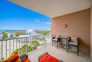 A balcony with a view of the beach, a table with chairs, and a small rug. - The Dunes 503 1 Bedroom Condo (Gulf Shores)