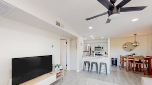 A modern living room with a flat-screen TV, a ceiling fan, and a dining area with wooden furniture. - Villa Sunrise 1 Bedroom Condo by RedAwning (Scottsdale)