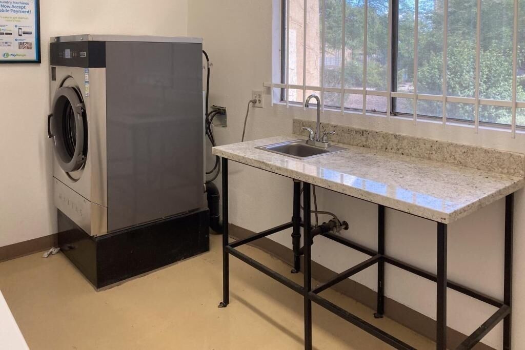 A compact laundry room with a washing machine, a sink, and a window with a view of greenery.