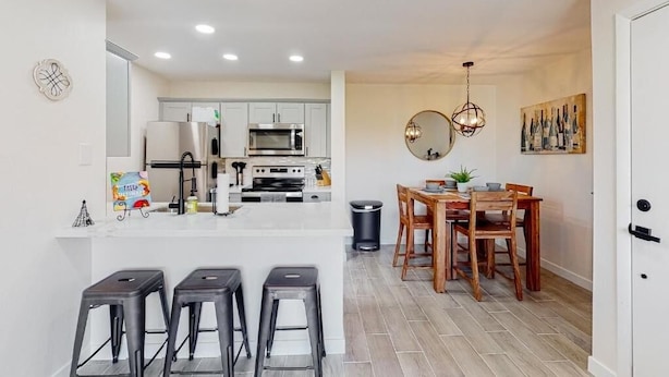 A modern kitchen with white cabinets, a central island, and a dining area with wooden chairs and a table. - Villa Sunrise 1 Bedroom Condo by RedAwning (Scottsdale)