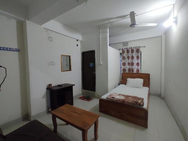 A bedroom with a bed, a desk, a chair, and a ceiling fan. - Hotel Labbaik Farmgate (Dhaka)