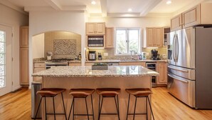 A modern kitchen with granite countertops, stainless steel appliances, wooden cabinets, and a large island with bar stools. - Private, Serene Mt Lookout 5B Retreat w/Garage & EV Charger (Cincinnati)