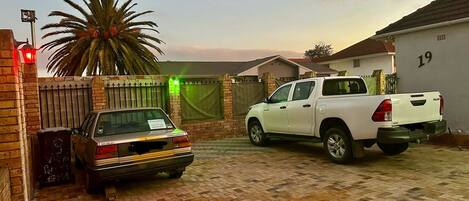 A gated driveway with a white pickup truck parked on the right and a silver sedan on the left.