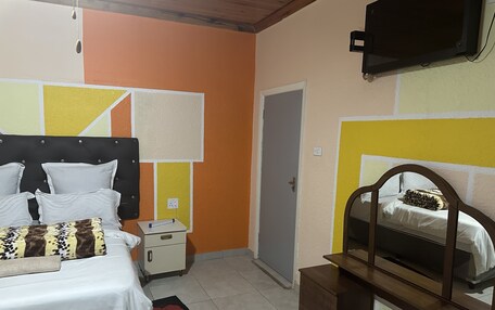 A bedroom with a bed, bedside table, dresser, mirror, and a door.