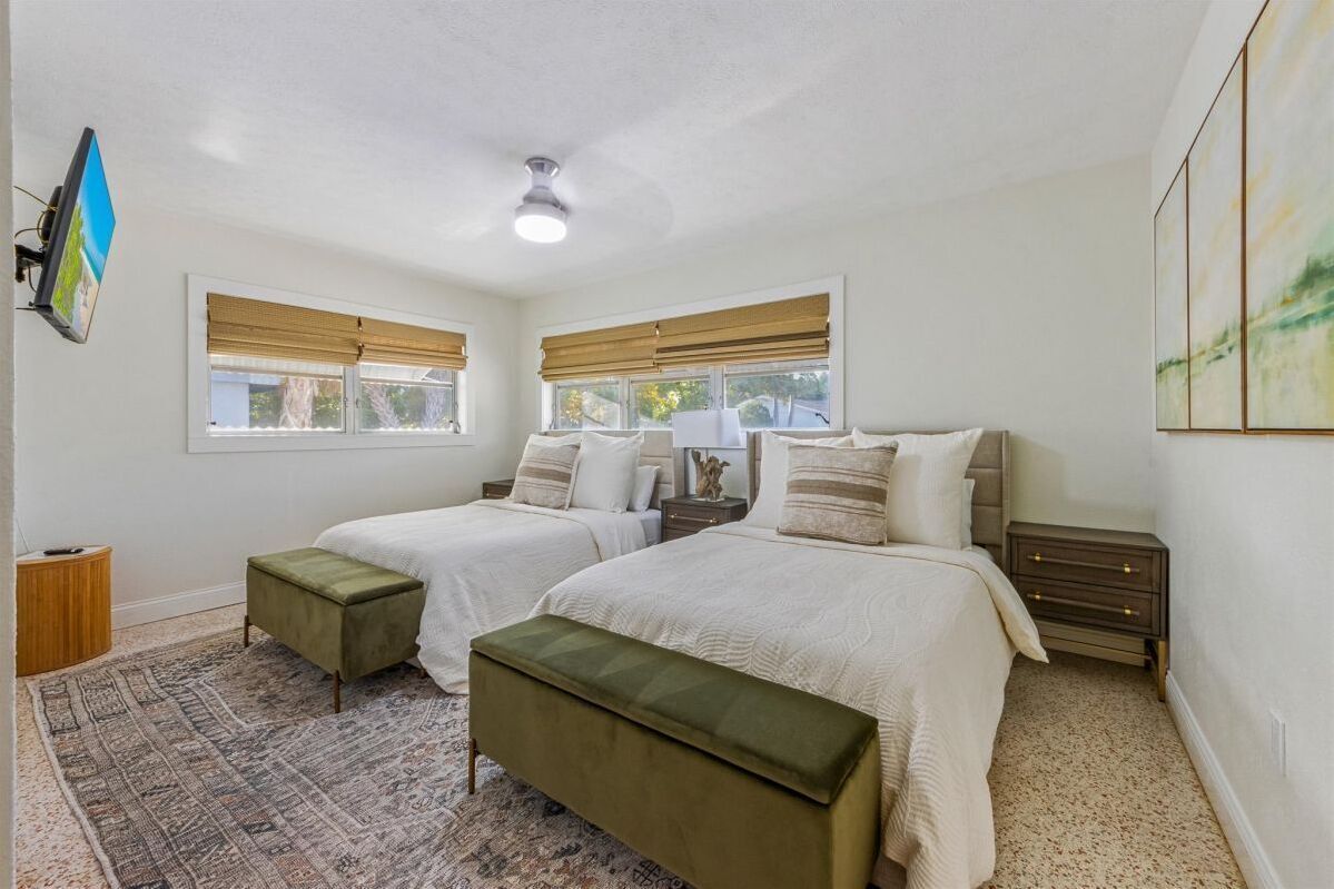 A bedroom with two beds, a ceiling fan, a rug, and artwork on the walls.