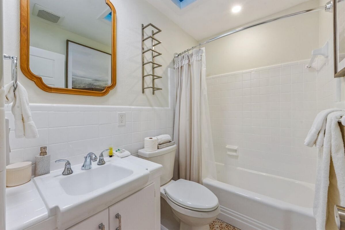 Une salle de bain avec un lavabo blanc, deux robinets, des toilettes, une baignoire et un rideau de douche.