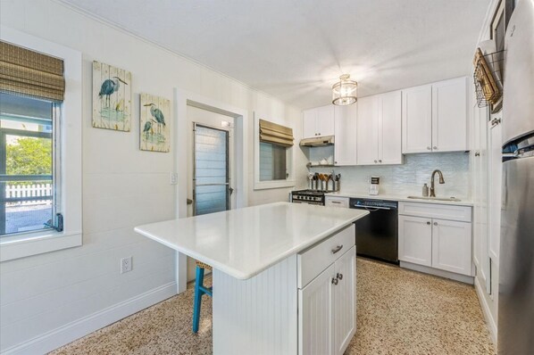 A kitchen with white cabinets, a central island, a dishwasher, and a stainless steel refrigerator. - Tranquil Palm: Perfect north-end location (Anna Maria)