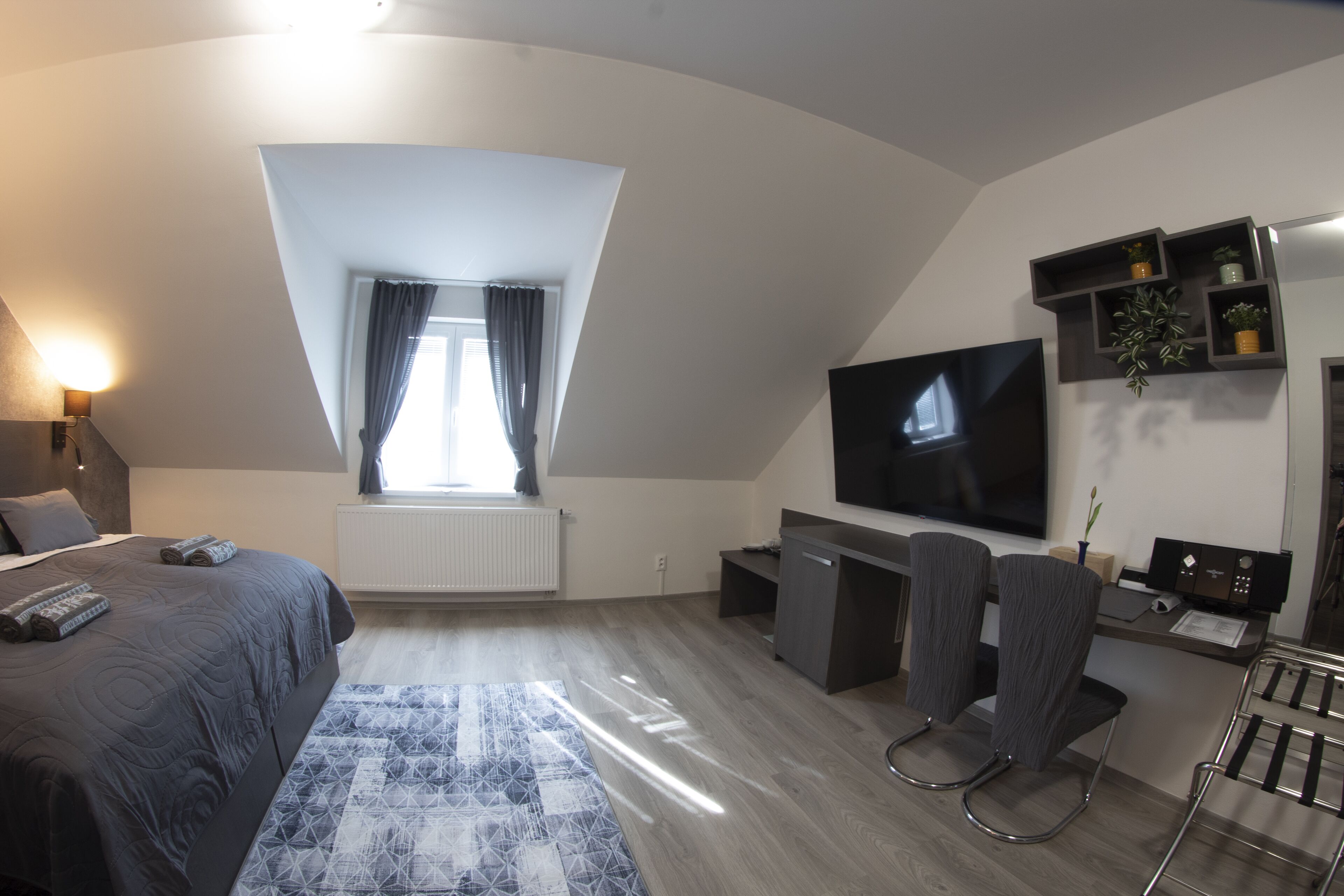 A modern hotel room with a large bed, a desk, a chair, a TV, and a window with curtains.