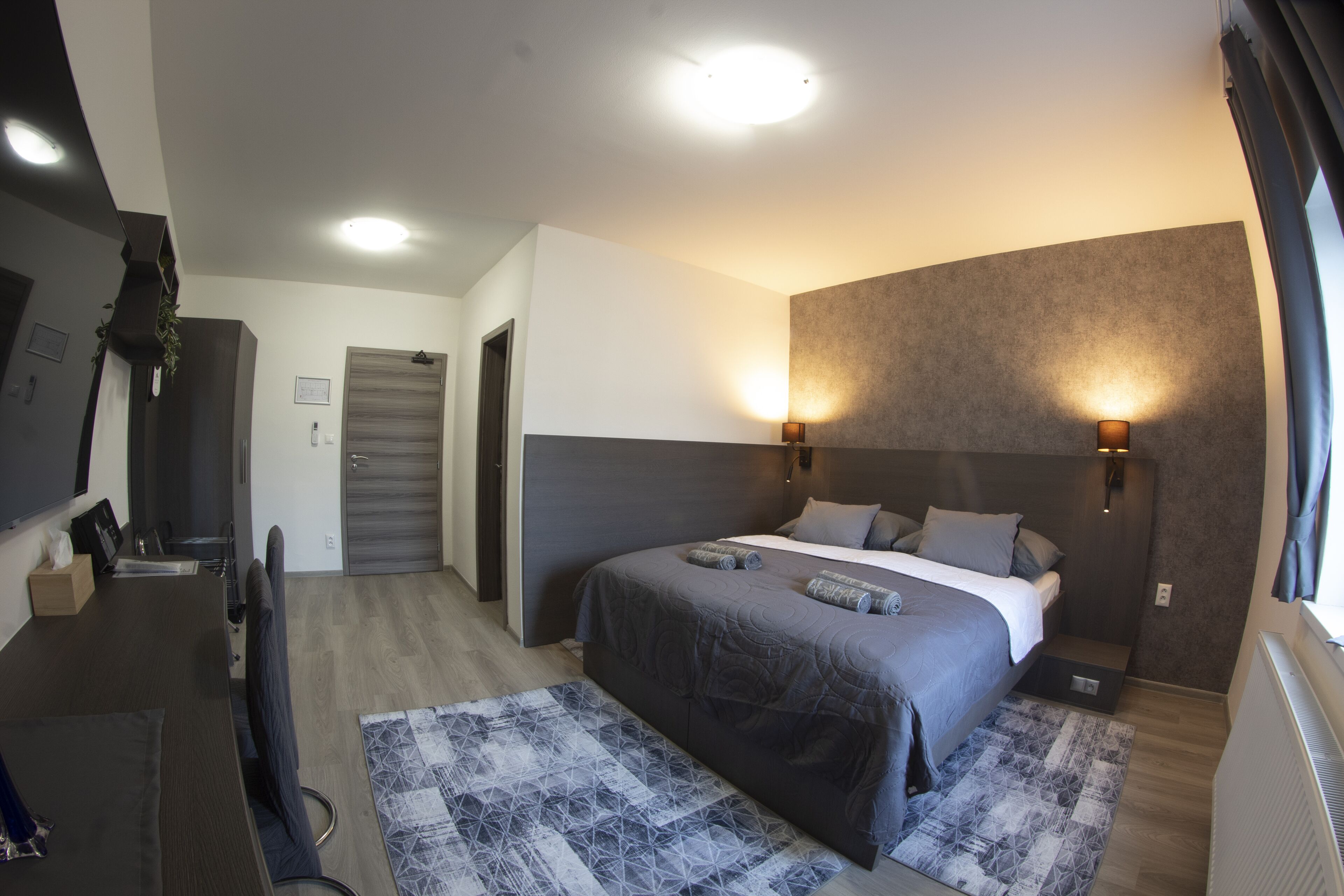 A modern bedroom with a bed, bedside lamps, a desk, and a patterned rug.