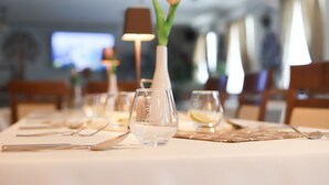 A dining table set with a vase of water and a single tulip, glasses, and cutlery. - VALLA penzión&reštaurácia (Malacky)